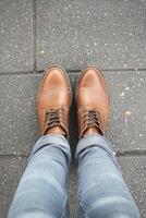 Casual male legs dressed in denim jeans and brown leather shoes while standing on a textured pavement in a vibrant urban setting photo