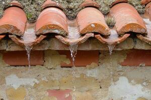 Water dripping from a traditional terracotta roof during rainfall in a rural setting photo