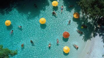 Aerial view of people swimming in a turquoise pool, surrounded by umbrellas and trees photo