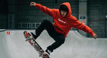 Asian skateboarder performs trick in skatepark wearing red hooded sweatshirt photo