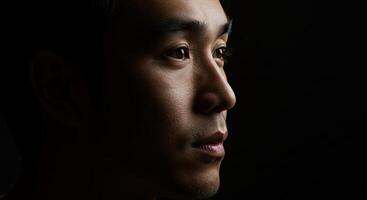 Thoughtful Asian man in profile with dramatic lighting and dark background photo