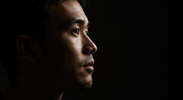 Thoughtful Asian man portrait in profile with dramatic lighting on black photo
