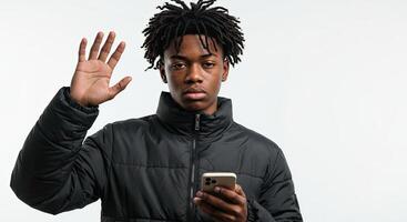 Young man in winter coat using smartphone with hand raised to stop photo