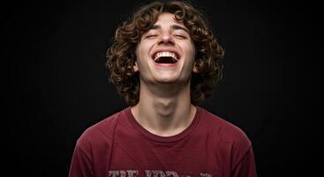 Young man with curly hair laughing joyfully against a dark background photo