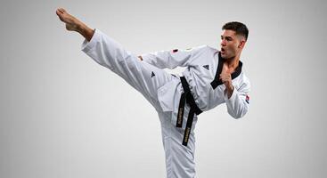Male Taekwondo athlete in action kicking with power and precision in studio photo