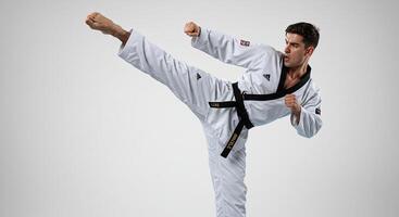 Male taekwondo athlete in uniform performing a kick in studio shot photo