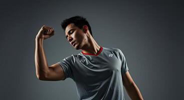 Muscular Asian man flexing bicep in sportswear against gray backdrop photo
