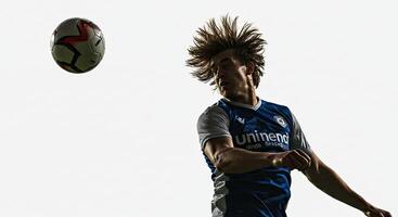 Soccer player heading the ball with determination against a bright background. photo