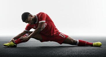 Soccer Player Stretching On Ground Before Training Session Against White Background photo