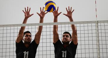 Two male athletes blocking a volleyball over the net during a competitive match photo