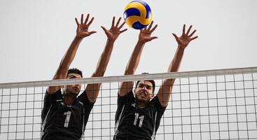 Two male volleyball players blocking a ball over the net during a match photo