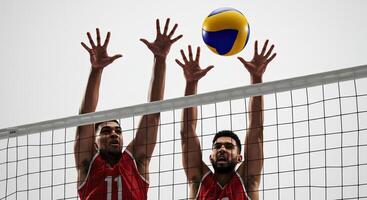 Two male volleyball players jumping to block a spike over the net in a match photo