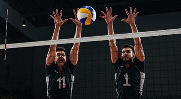Two male volleyball players jumping to block a volleyball during a match game photo