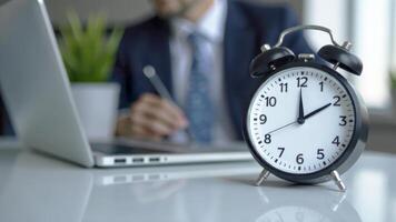 Clock on desk with businessman working on laptop, emphasizing time management and productivity in a modern office setting, time management concept photo