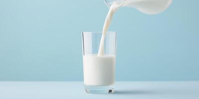 Fresh milk being poured from a glass jug into a clear glass on a light blue background, showcasing the creamy texture and refreshing nature of the beverage in a bright setting photo