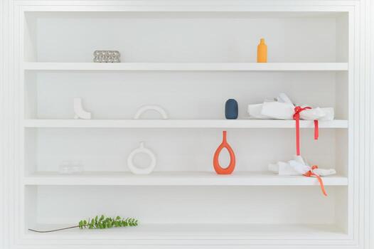Minimalist white shelf featuring simple decor items including vases and decorative objects arranged in clean style with touch of color and natural greenery for calm atmosphere photo