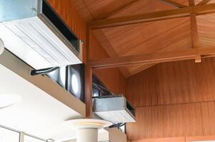 Close up view of modern HVAC duct system installed against wooden vaulted ceiling with exposed beams in bright interior space showing architectural details and ventilation components photo