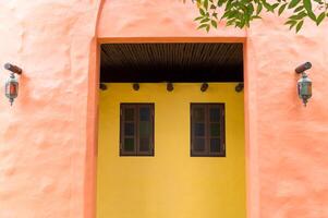 Moroccan inspired doorway featuring stained glass panes and vibrant yellow walls creating colorful and inviting entrance with rustic lanterns and natural wooden ceiling beams photo