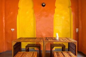 Bright room interior with yellow and orange walls featuring wooden tables and art, creating warm and inviting atmosphere with simple modern furniture and soft lighting photo