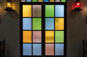 Colorful stained glass window with intricate patterns and warm lighting from adjacent lanterns creates cozy and inviting atmosphere in room photo