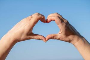 Two hands making a heart shape with a blue sky in the background photo