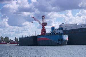 Cargo ship being loaded at a busy dock in the port with cranes and clouds in the backdrop photo