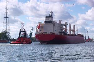 Large cargo ship navigates the waterway with assistance from a tugboat under a bright sky and scattered clouds photo