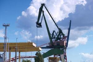 Large crane operating at a construction site near the waterfront under a bright blue sky with clouds in the background photo