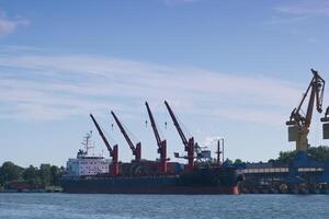 Cargo ship docks at busy port with large cranes lifting containers on a clear sunny day photo