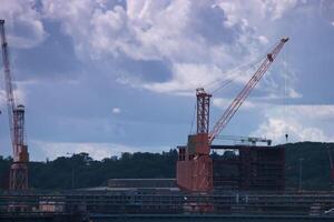 Construction cranes working on a large building project near a waterfront location during cloudy weather in the afternoon photo