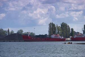 Red cargo ships docked at a busy industrial port with coal piles and trees in the background photo