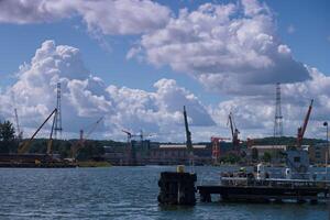 Construction activity at waterfront site with cranes and clouds in the background during midday photo