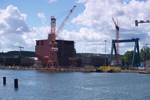 Construction of a large ship at a shipyard in bright daylight with cranes and scaffolding present in the background photo