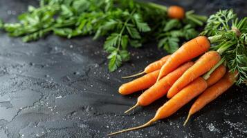 Bunch of bright orange carrots with lush green tops resting on a rustic surface photo