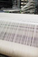 Weaving loom with white threads in a textile factory, showing industrial fiber alignment process. photo