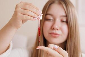 Girl applying red face serum with pipette as part of daily skincare routine at home. photo