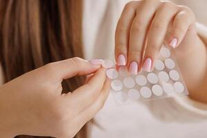 Hands removing acne patch from sheet, skincare routine concept with soft pink manicure close-up. photo