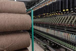 Brown yarn spools beside automated spinning machine with colorful thread bobbins in a textile plant. photo