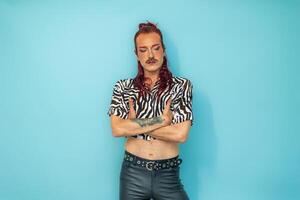Non-binary person with arms crossed looking down on blue background photo