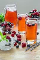 Colorful berry drinks filled with ice cubes and adorned with fresh berries create a vibrant display on a wooden surface, accompanied by mint leaves for added freshness. photo