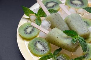Chilled kiwi icecream popsicles are presented on a golden plate surrounded by ice cubes and fresh kiwi slices, creating a refreshing summer delight at a gathering. photo