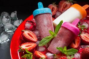 vistoso fresa hielo crema y Paletas de hielo descanso en un vibrante cuenco lleno con aplastada hielo y Fresco fresas, creando un Perfecto verano postre. el escena invita disfrute. foto