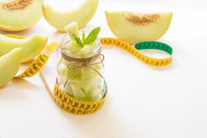 Jar with melon pieces on burlap napkin near cut slices of melon and centimeter right empty place for text on a white background. Pieces of melon in a jar. Horizontal. Daylight. photo