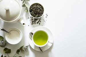 Bright green tea prepared in a simple cup alongside loose tea leaves, sugar bowl, and eucalyptus branches creating a calming atmosphere in a minimalist setting. photo
