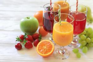 Colorful array of refreshing fruit juices showcases orange, red, and green beverages alongside fresh fruits on wooden surface, inviting taste and enjoyment during warm summer days. photo