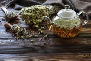 Tea in glass teapot, surrounded by fresh herbs and dried flowers on weathered wooden table, creating warm and inviting atmosphere for relaxation and enjoyment. photo