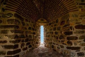 A well-worn stone wall with a narrow passage provides a picturesque view of a distant sea horizon photo