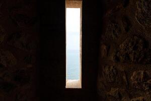Dimly lit ancient stone corridor with light streaming through an open door, evoking mystery and exploration. photo
