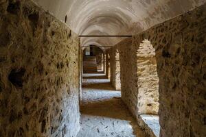 A long stone corridor featuring arched openings and natural light, evoking ancient architectural craftsmanship and historical ambiance. Ideal for themes of history, architecture, and heritage preservation. photo