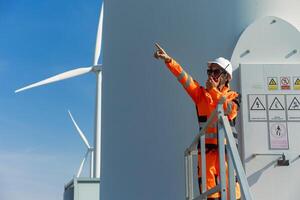 A man in an orange jacket pointing at a wind turbine photo